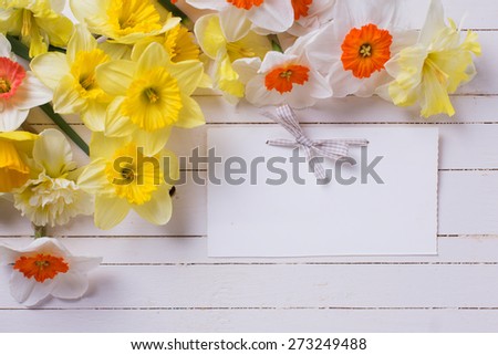 Border from colorful yellow, orange and white spring flowers and empty tag  on white  painted wooden planks. Selective focus. Place for text.