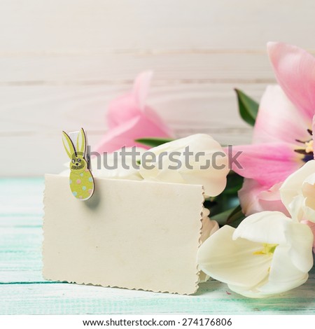 Postcard with fresh spring flowers and empty tag for your text on turquoise painted planks against white wall. Selective focus. Square image.