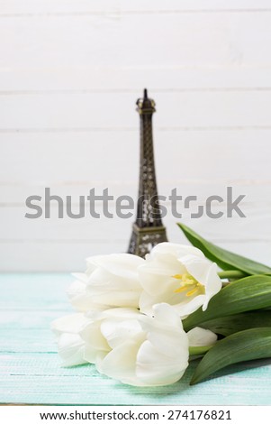 Postcard with fresh spring flowers and little Eiffel tower on turquoise painted planks against white wall. Selective focus.