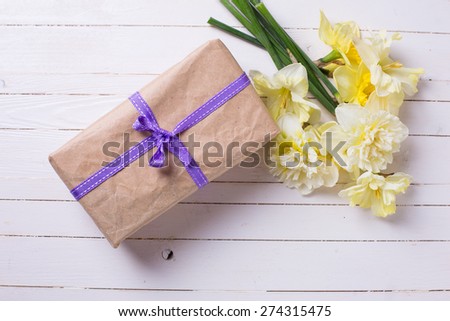 Box with present and spring flowers narcissus on white painted wooden planks. Selective focus.