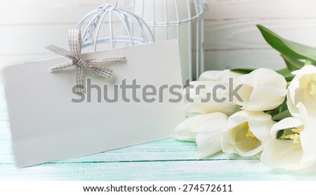 Postcard with fresh spring white flowers and empty tag for your text on turquoise painted planks against white wall. Selective focus. Toned image.