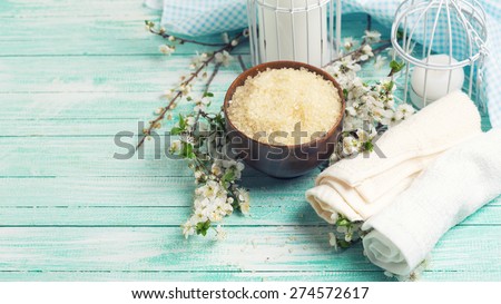 Spa and wellness setting. Sea salt in bowl, towels, candles and  flowering branches of trees on turquoise painted wooden background. Selective focus.Toned image.
