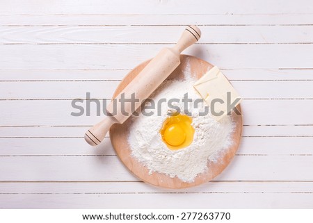 Ingredients for dough -  flour on wooden board, egg, butter  on white wooden background. Selective focus.