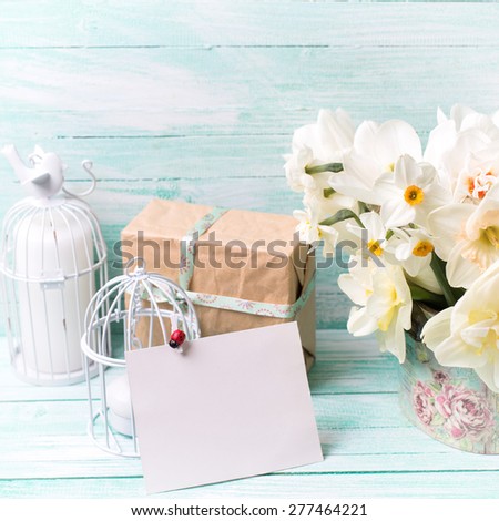 Background with colorful narcissus flowers , candles, box with present  and empty tag for text on turquoise painted wooden planks. Selective focus. Place for text. Square image.