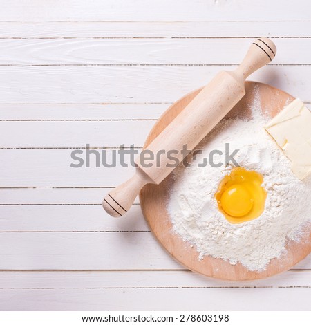 Ingredients for dough -  flour on wooden board, egg, butter  on white wooden background. Selective focus. Square image.