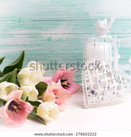 Fresh  spring white and pink tulips flowers,  decorative heart and candles  on white  painted wooden planks against turquoise wall. Selective focus. Square image.