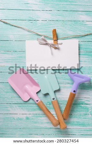 Tools for children for playing in sand and tag on clothes line on turquoise  painted wooden planks. Place for text. Vacation, holiday, summer background.