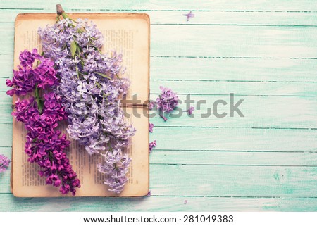Background  with fresh lilac flowers on open vintage book  on turquoise painted wooden planks. Selective focus. Place for text. Toned image.