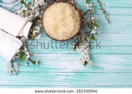 Spa and wellness setting. Sea salt in bowl, towels and  flowering branches of trees in ray of light on turquoise painted wooden background. Selective focus.