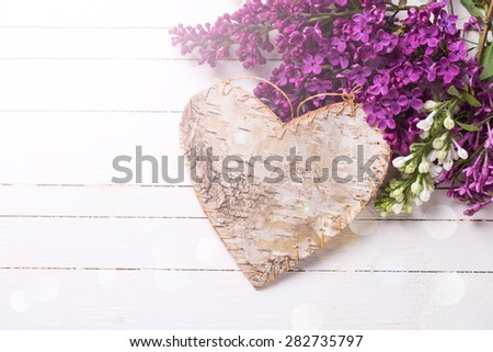 Fresh white and violet lilac flowers and decorative rustic heart in ray of light  on white painted wooden planks. Selective focus. Place for text.