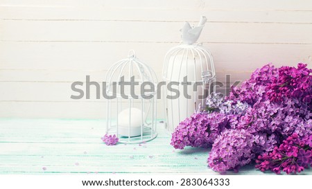 Background  with fresh lilac flowers and candles in decorative bird cages  on turquoise painted wooden planks against white wall. Selective focus. Place for text. Toned image.