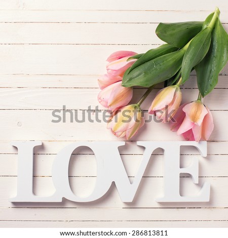Fresh  spring  pink  tulips and word love  on white  painted wooden background. Selective focus. Square image.