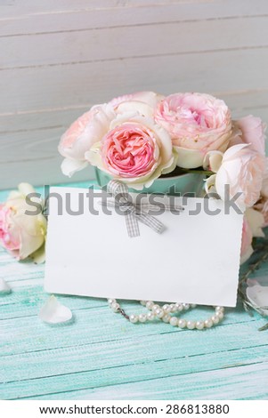 Postcard with  sweet roses flowers and empty tag for your text on turquoise painted wooden background against white wall. Selective focus.