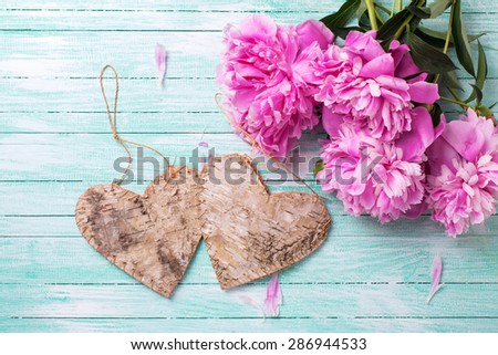 Wedding background. Splendid  pink  peonies flowers and two decorative heart on turquoise painted wooden planks. Selective focus is on flowers.