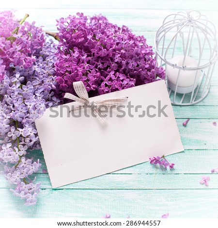 Background  with fresh lilac flowers,  candle and empty tag on turquoise painted wooden planks. Selective focus. Place for text. Square image.