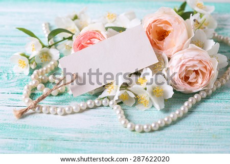Sweet pastel roses and jasmine flowers and empty tag  on turquoise wooden background. Place for text. Selective focus.