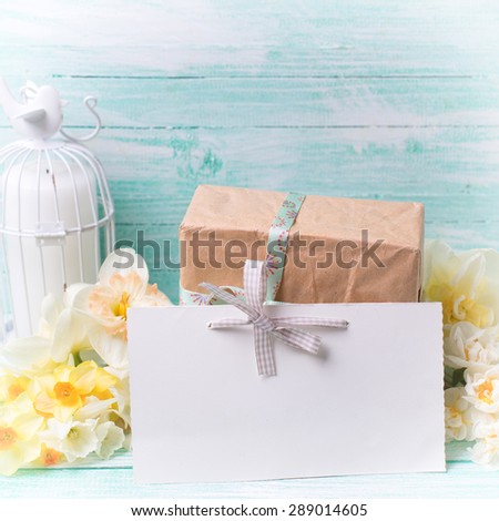 Narcissus flowers , empty tag for text , candle, box with present  on turquoise painted wooden planks. Selective focus. Place for text. Square image.