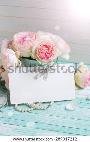 Postcard with  sweet roses flowers and empty tag for your text in ray of light on turquoise painted wooden background against white wall. Selective focus.