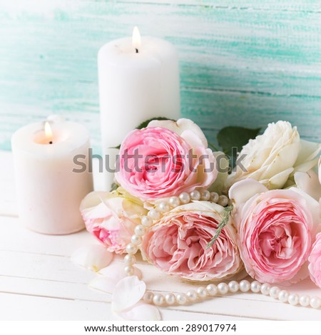 Background with sweet pink roses flowers and candles  on white painted wooden background against turquoise wall. Selective focus. Square image.