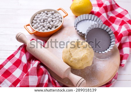 Dough  on wooden board,  tartlet tins,  ceramic  baking beans  on white wooden background. Selective focus.