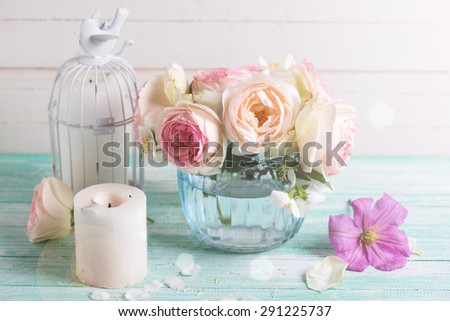 White roses, clematis and jasmine flowers  in vase and candles in ray of light  on turquoise wooden background against white wall. Place for text. Selective focus.