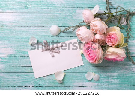 Postcard with fresh roses flowers and empty tag for your text on turquoise painted wooden background. Selective focus.