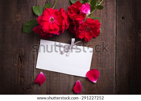Empty tag and fresh red roses  on aged wooden background. Selective focus id on tag. Place for text. Toned image.