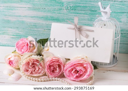 Postcard with sweet roses flowers and empty tag for your text on white painted wooden background against turquoise wall. Selective focus.