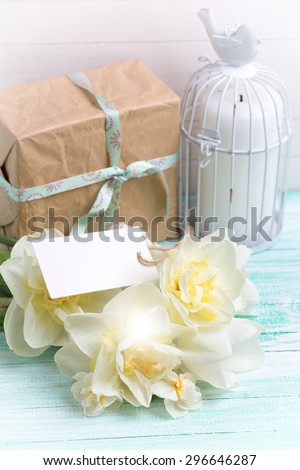 Postcard with fresh  daffodils flowers, candle and gift box  and tag on turquoise painted wooden planks against white wall. Selective focus is on flowers. Place for text. Toned image.