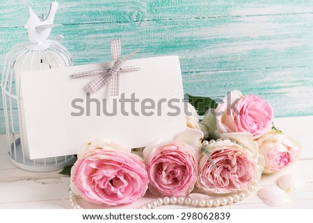 Postcard with sweet roses flowers and empty tag for your text on white painted wooden background against turquoise wall. Selective focus. Toned image.
