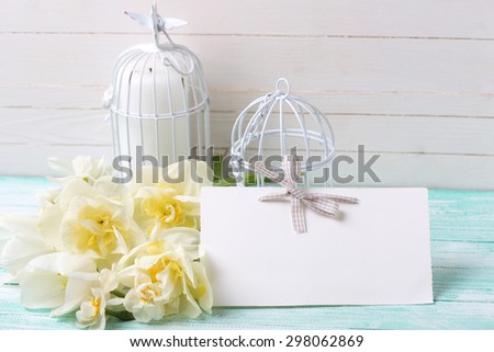 Background with fresh spring flowers, tag and candles in decorative bird cages on turquoise painted planks against white wall. Selective focus is on tag.