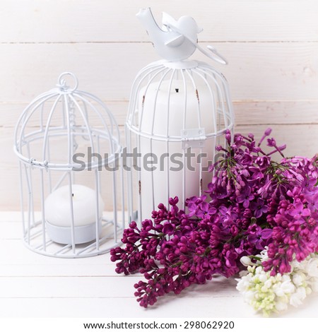 Fresh white and violet lilac flowers and candles on white painted wooden planks. Selective focus. Square image.