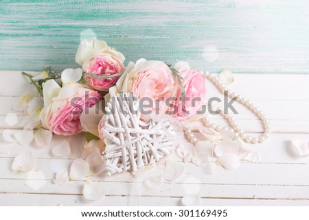 Decorative heart and sweet pink roses  in ray of light on white background against turquoise wall. Selective focus. Place for text.