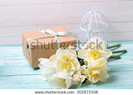 Postcard with fresh  daffodils flowers, candle and gift box on turquoise painted wooden planks against white wall. Selective focus.