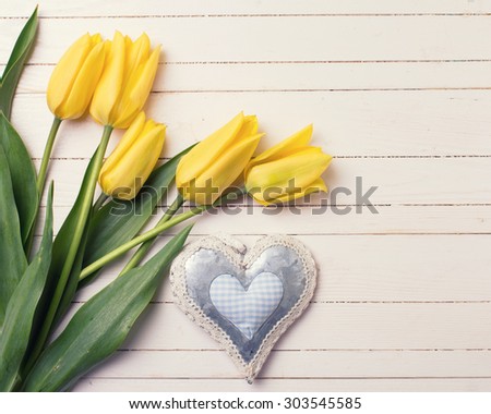 Fresh aromatic  yellow tulips flowers  and decorative heart on white painted wooden background. Selective focus. Place for text. Toned image.