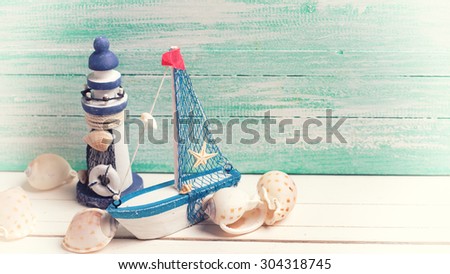 Decorative lighthouse, sailing boat and marine items on wooden background. Sea objects on wooden planks. Selective focus in on boat. Place for text. Toned image.