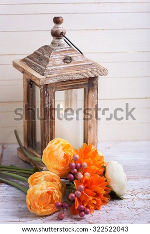 Autumn still life photo with flowers  in yellow colors and candle in lantern on wooden background. Selective focus. Toned image.