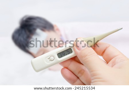Mother holding digital thermometer and sick little boy in bed