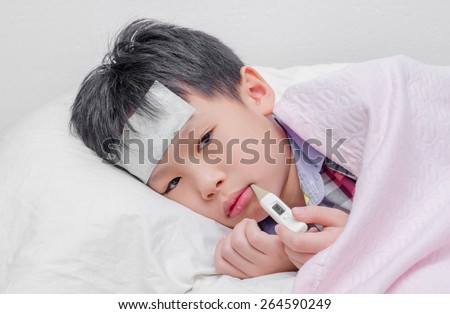 Little sick boy lying on bed with digital thermometer in mouth