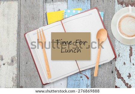 Time for lunch on notebook with spoon and coffee cup on wood table