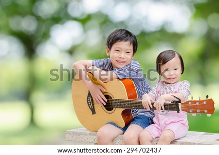 Asian boy and his younger sister play guitar and sing in garden