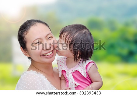 Little Asian girl kissing her mom in garden