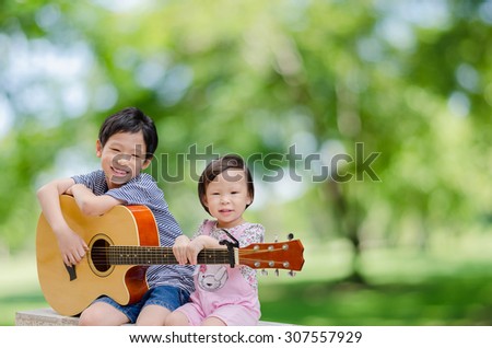 Asian boy and his younger sister play guitar and sing in garden