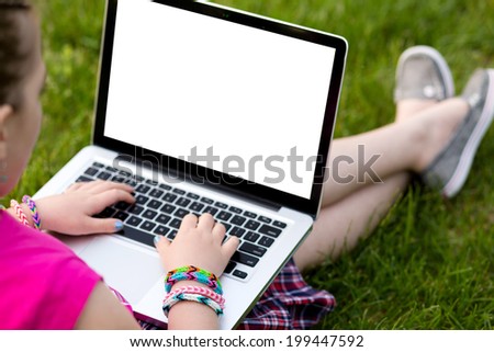 Young girl wearing loom rubber bracelets using the laptop, sitting on the grass in the park. Back to school, young fashion, life style concept