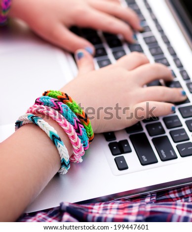 Young girl wearing loom rubber bracelets using the laptop, sitting on the grass in the park. Back to school, young fashion, life style concept