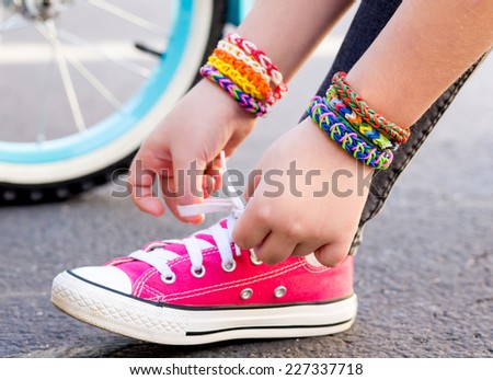 Young girl wearing loom bracelets, lacing sneakers. Young fashion, outdoors, friendship, crafts, and lifestyle concept. Bright tones. Shallow depth of field.