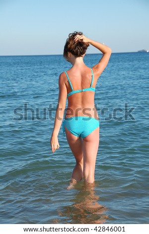 slim back of young woman standing in water against blue sea