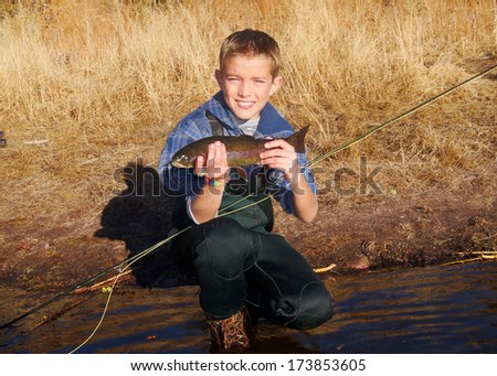 Boy fly fishing - Child, fish (Rainbow Trout), and fly rod or pole next to a stream