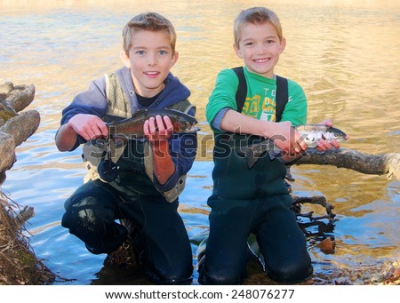 Children fishing - brothers and friends holding prize fish they caught fly fishing in a clear stream (Rainbow Trout)