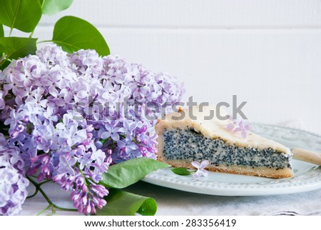 Slice of poppy seed cake with lilac flowers on white wooden background